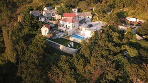 An aerial view of a large estate with multiple buildings, a swimming pool, and surrounding forested area. - House Marinka (Split)