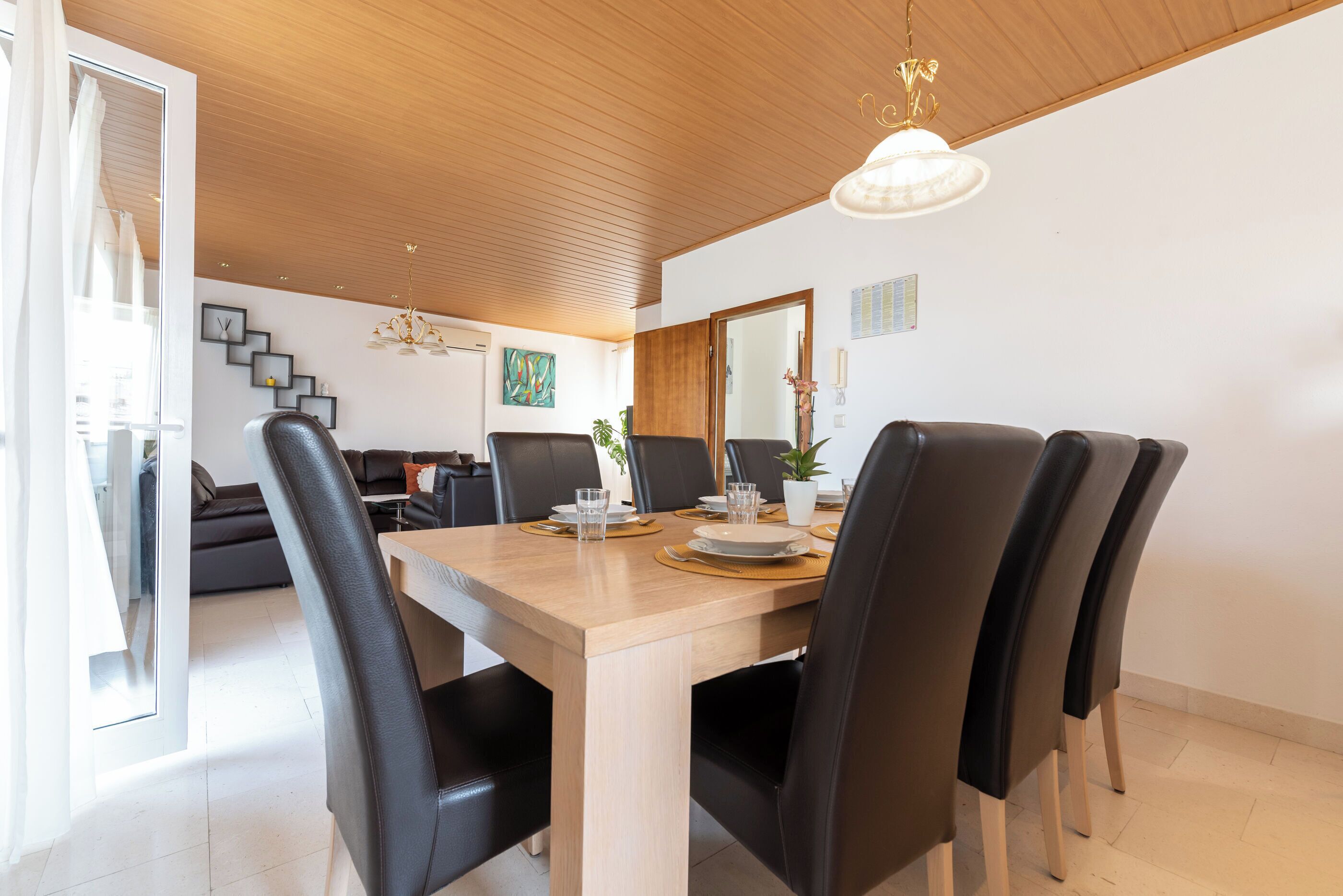 Un comedor con una mesa de madera, sillas negras y una araña.