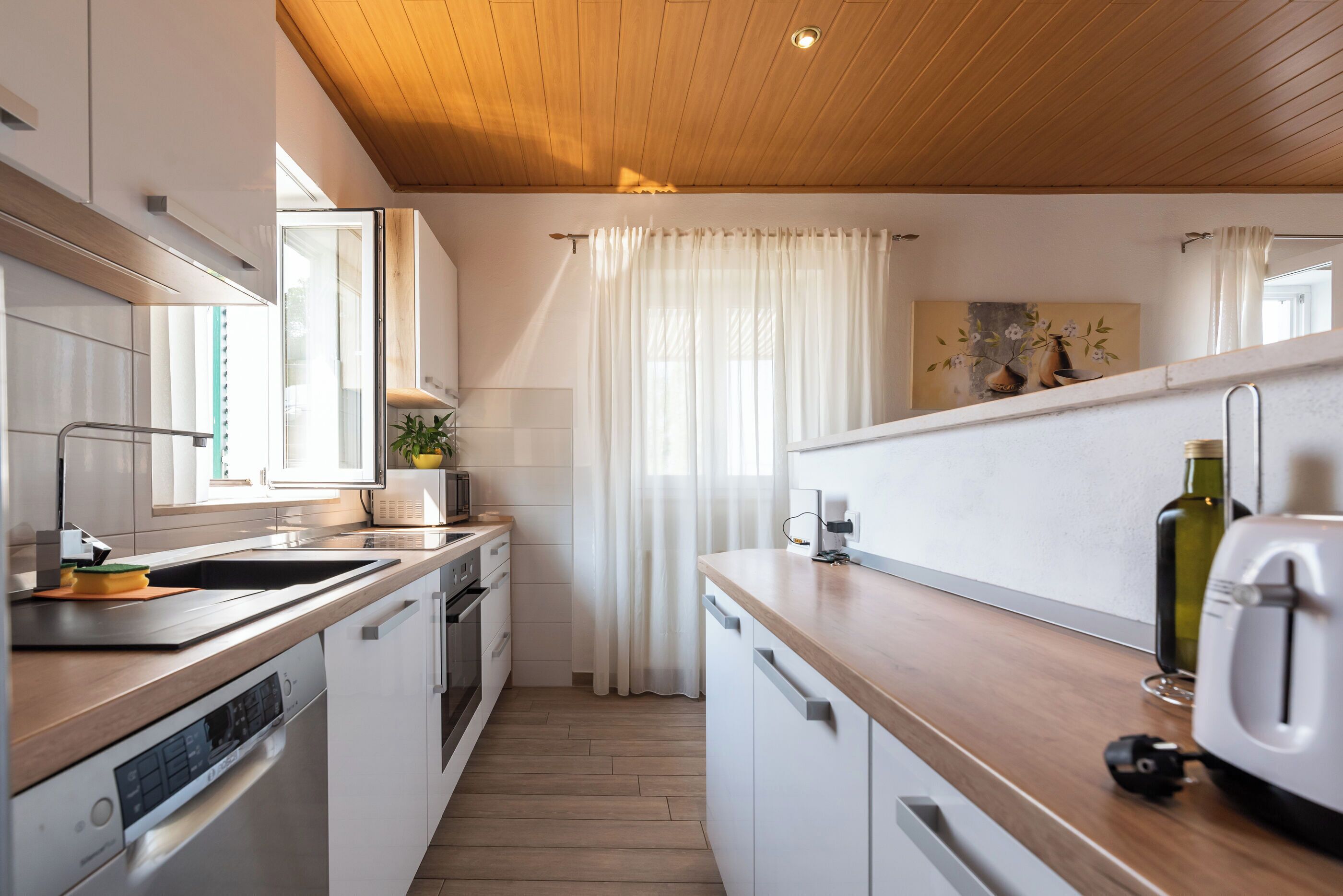 A modern kitchen with white cabinets, wooden countertops, a built-in oven, and a stainless steel sink.