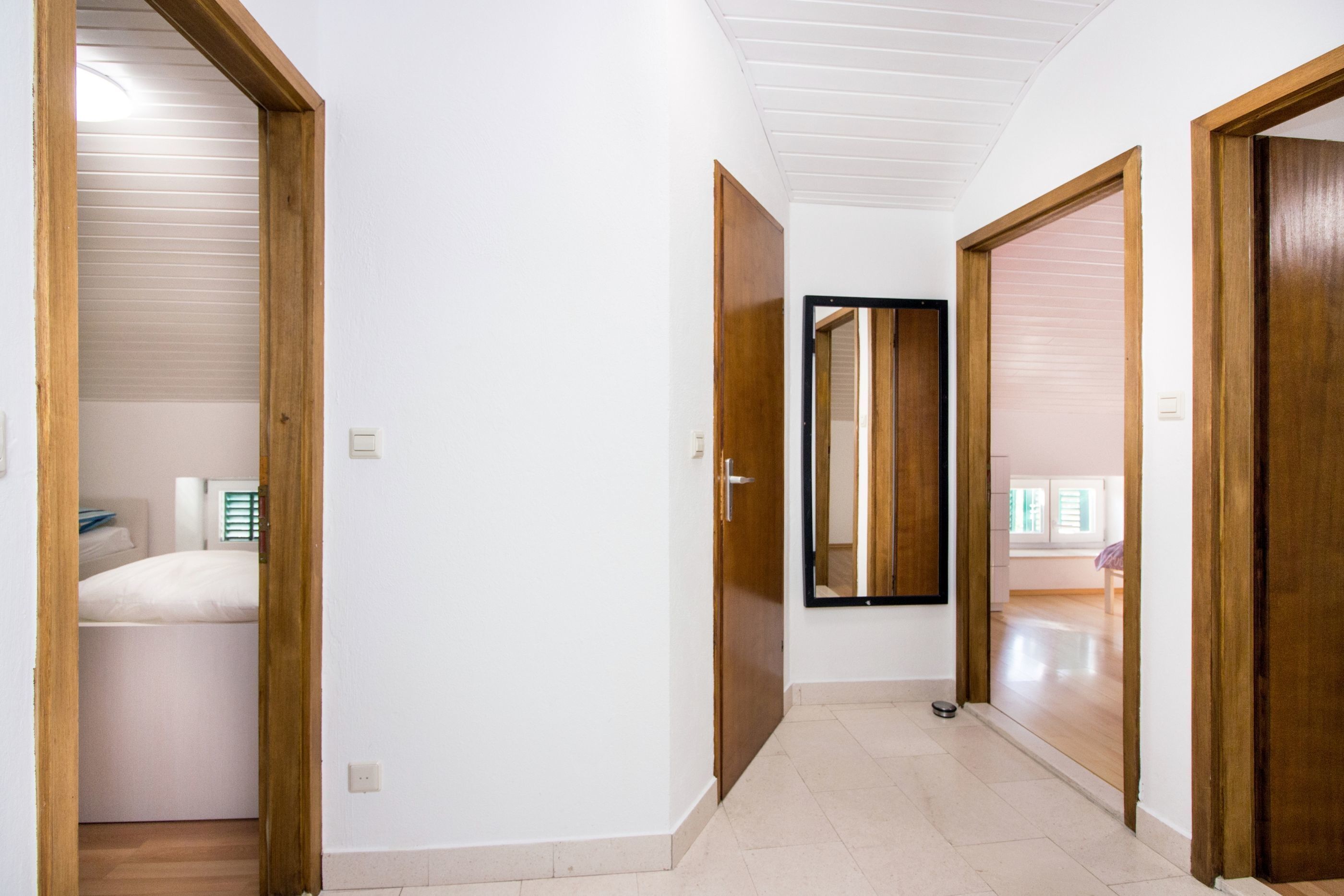 Un couloir avec des portes en bois, un lit dans la pièce de gauche et une fenêtre avec des stores.