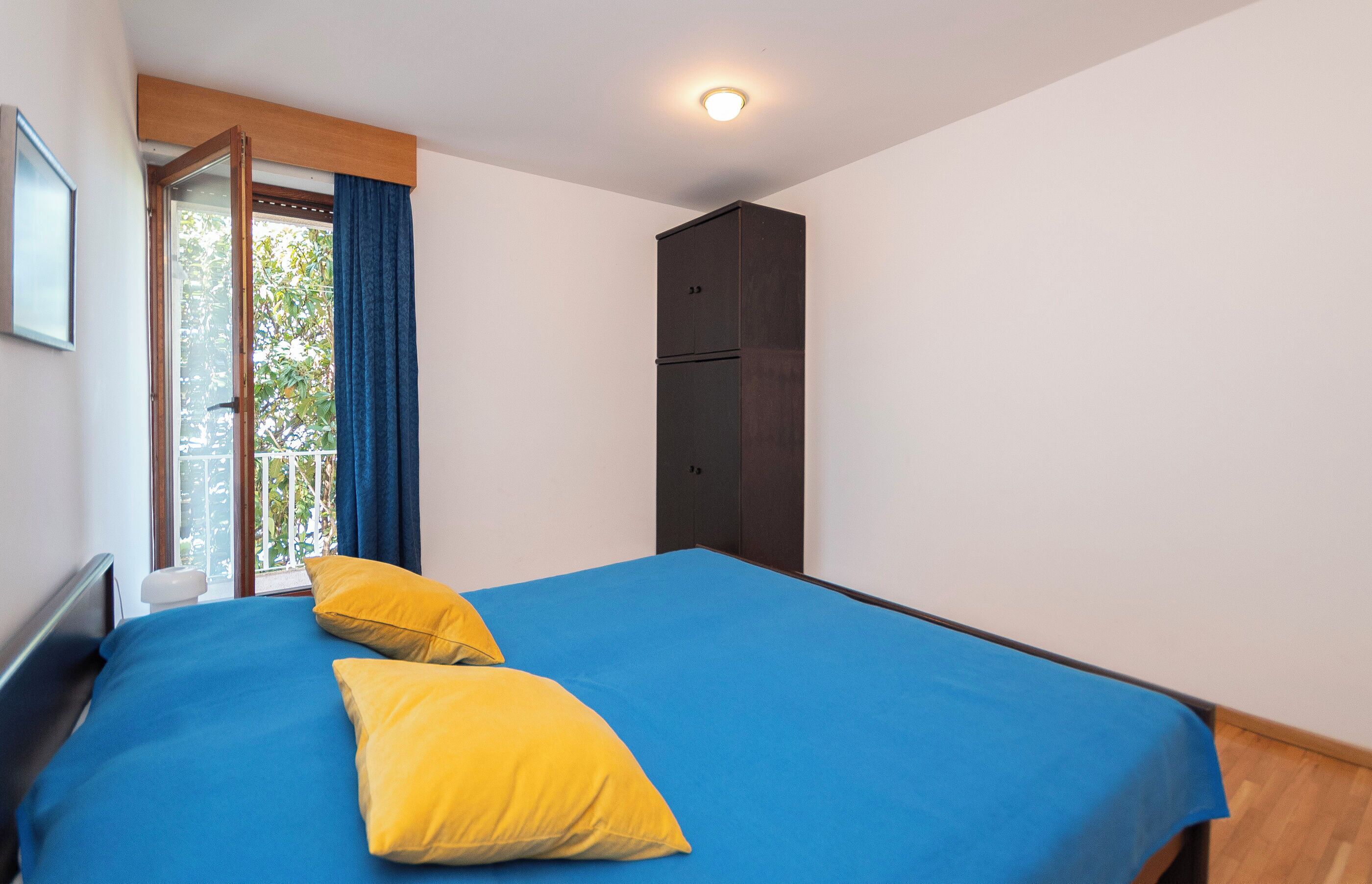 A bedroom with a bed, two yellow pillows, a dark wardrobe, and a window with blue curtains.