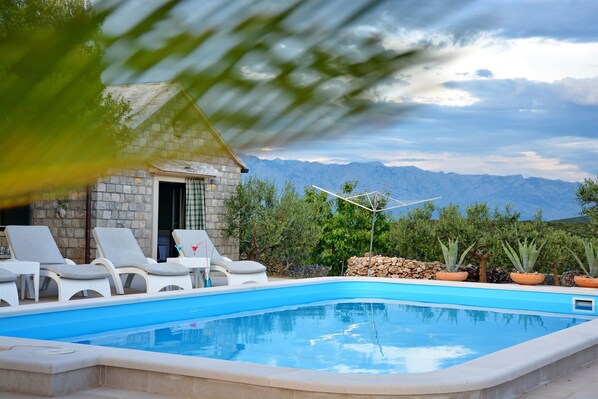 A swimming pool with lounge chairs, a stone building, and a mountainous backdrop. - House Sweet Dreams (Selca)