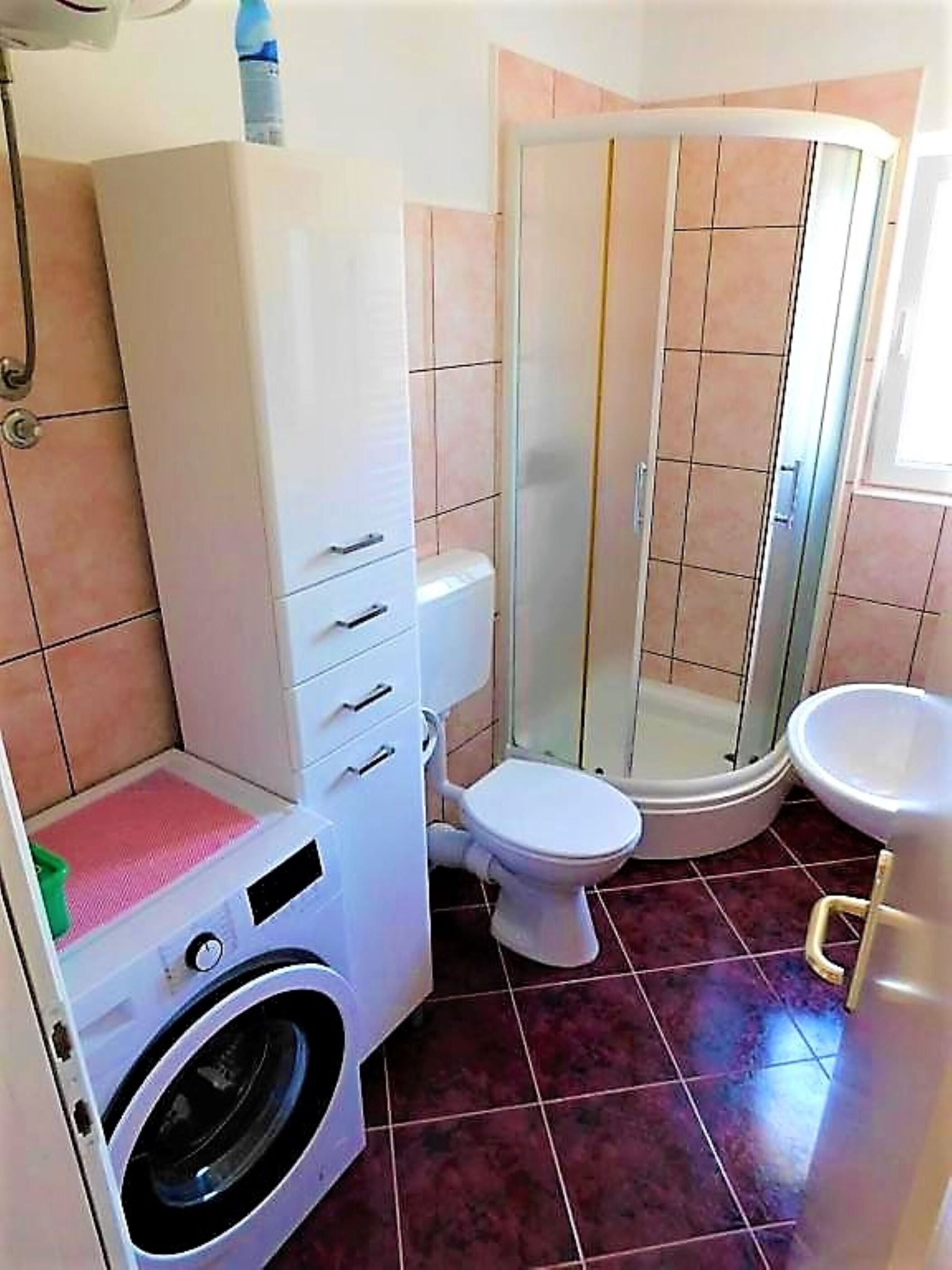 Et lille badeværelse med vaskemaskine, toilet og bruser.