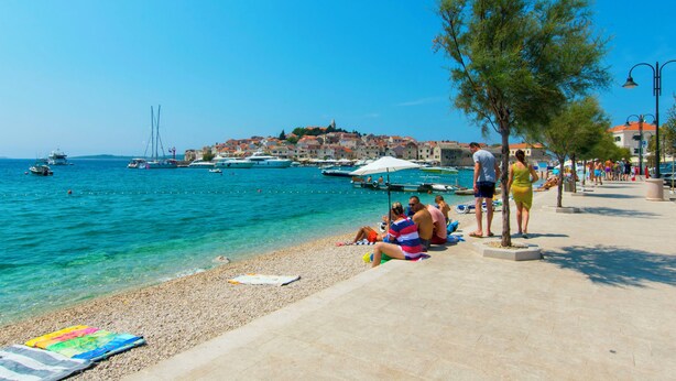 A coastal town with a pebbled beach, boats, and a historic building in the background. - Apartments Huljev (Primosten)