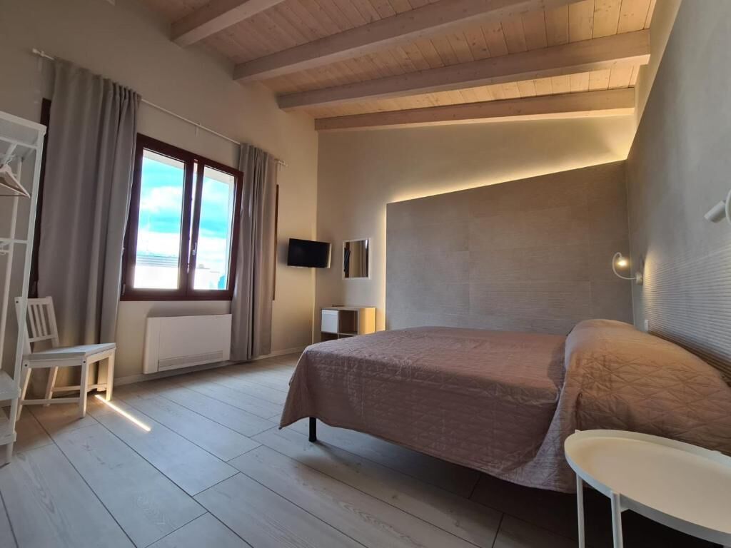 A bedroom with a bed, a chair, a small table, a TV, and a window with curtains.