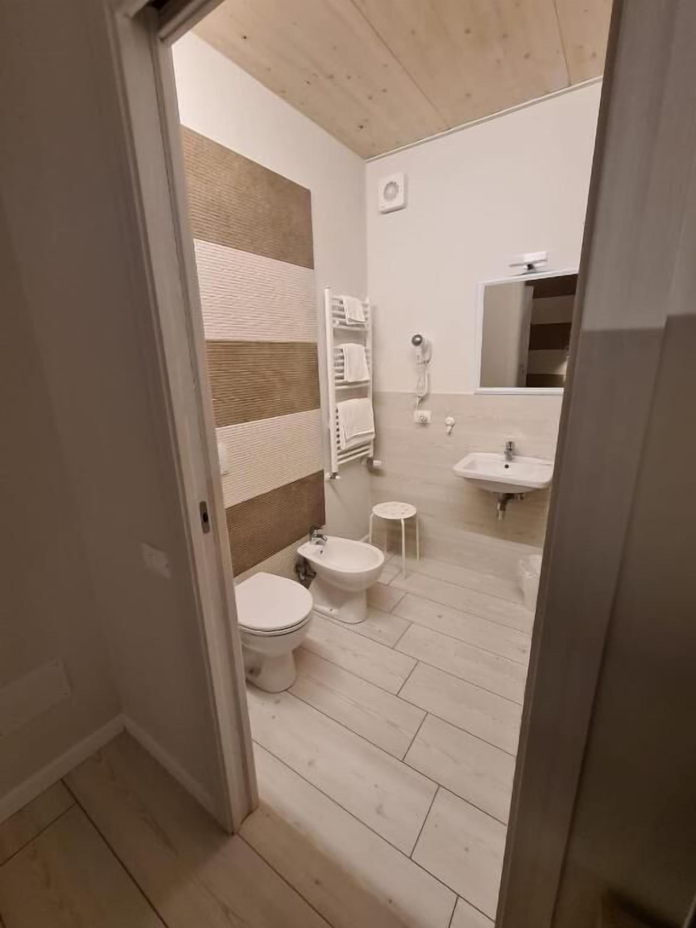 A bathroom with a wooden floor, a white sink, and two toilets.