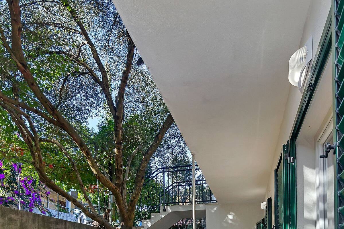 A balcony with stone walls, metal chairs, and a view of trees and buildings.