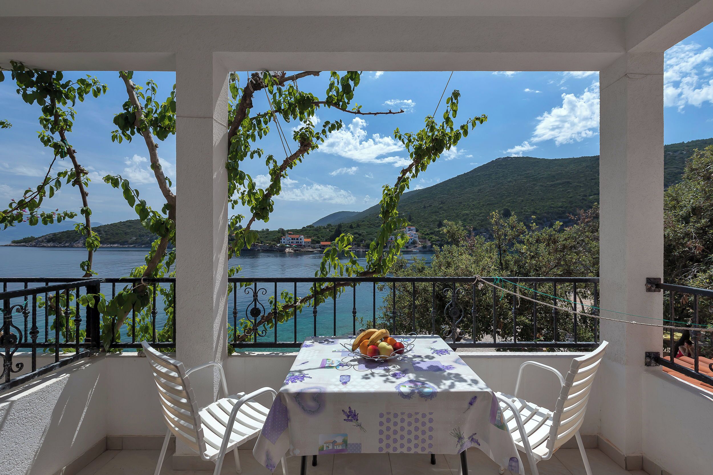 Un balcon avec une table dressée pour deux personnes, donnant sur une étendue d’eau et des collines.