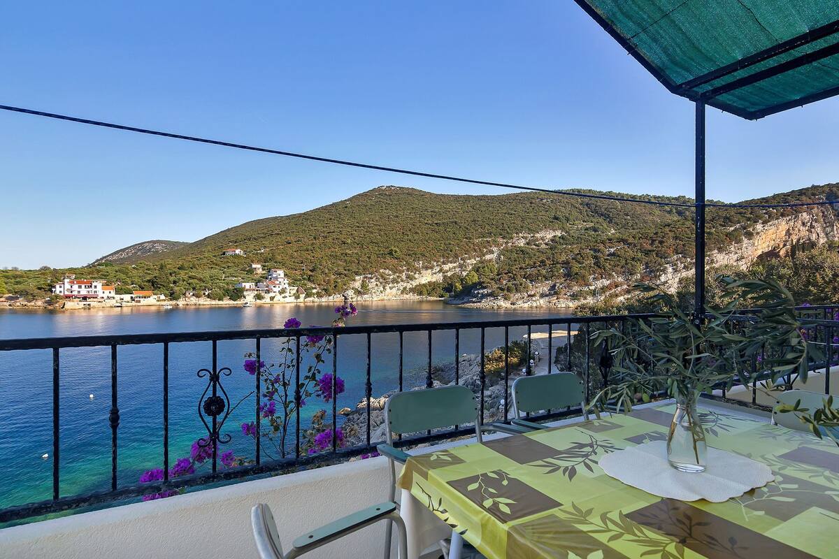 A balcony with a table and chairs overlooking a body of water and a mountainous landscape.