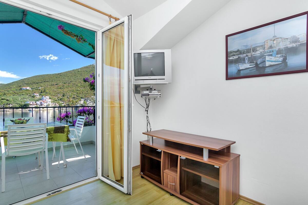 A balcony with a table and chairs, a sliding glass door, a TV, and a framed picture on the wall.