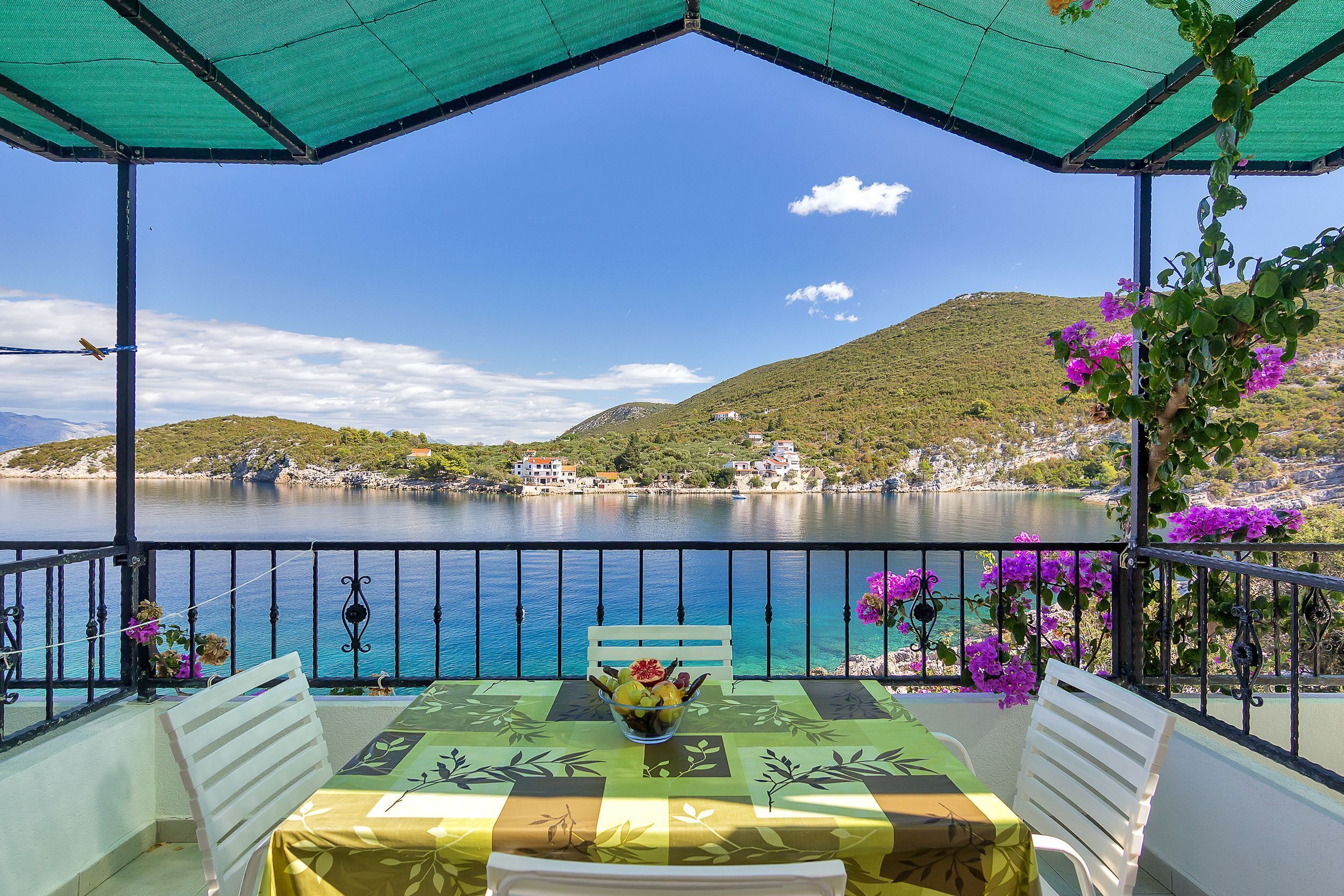 Un balcon avec une table dressée pour le dîner, donnant sur un lac et offrant une vue sur les montagnes en arrière-plan.