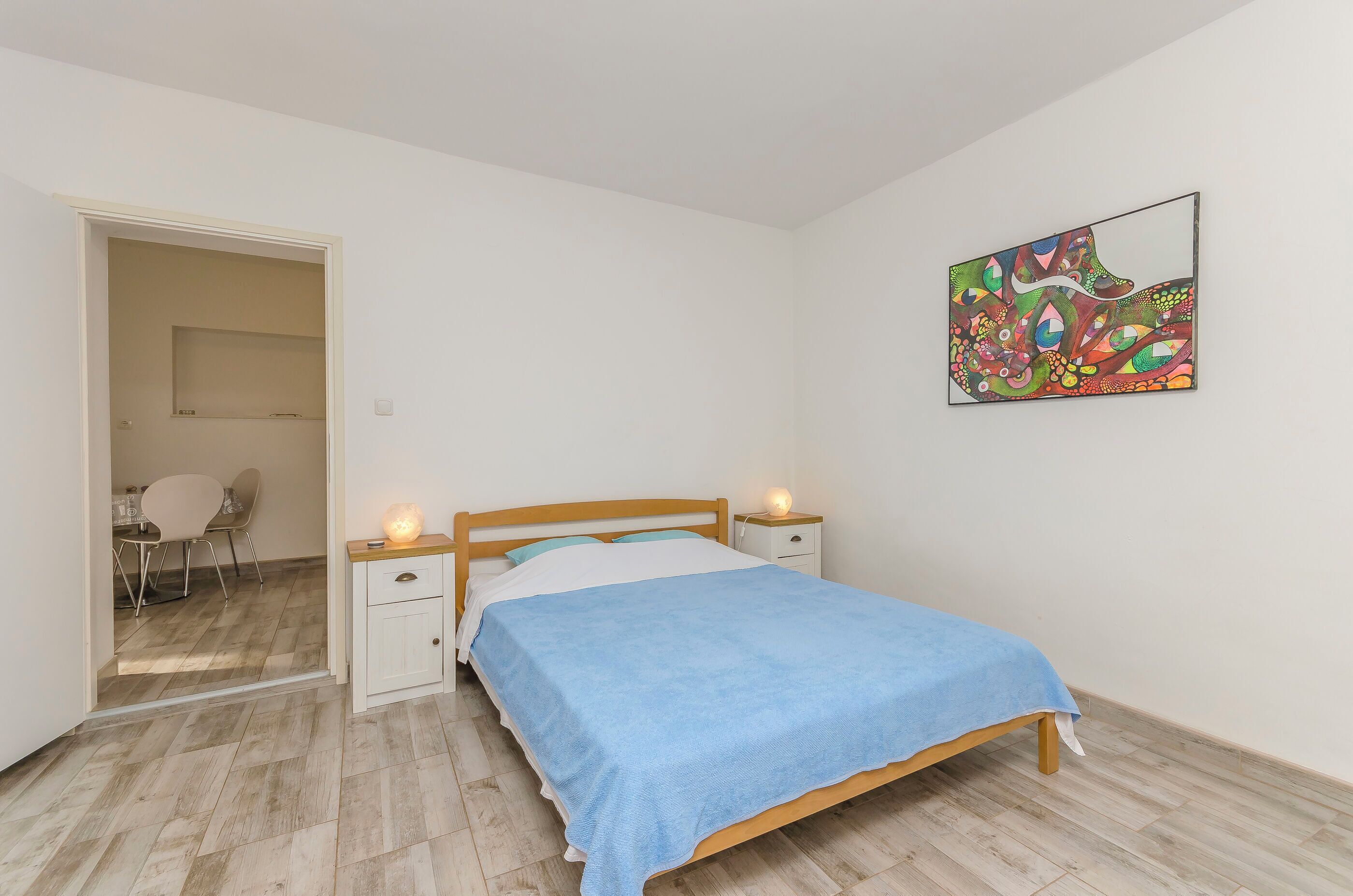 Une chambre à coucher comprenant un lit, des tables de chevet, un miroir et une porte donnant sur une autre pièce.