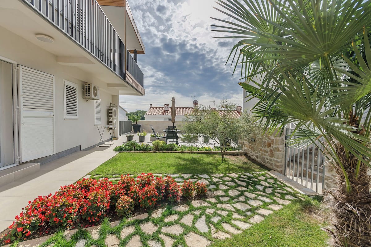 A courtyard with a white building, a palm tree, and red flowers.