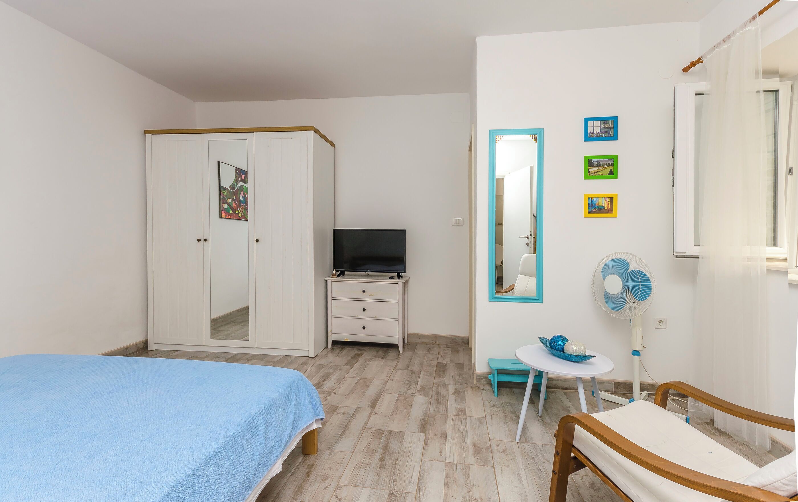 Ein Schlafzimmer mit Bett, Fernseher, Kleiderschrank, Spiegel und Ventilator.