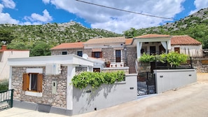 A two-story stone house with a red-tiled roof, a stone wall with a green vine, and a black gate. - House Ante (Starigrad)
