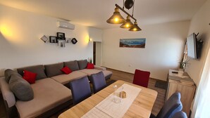 En moderne stue med sofa, spisebord og stole. Et billede hænger på væggen, og et fjernsyn er monteret der.