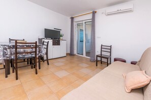 Un salon comprenant un canapé, un téléviseur, une table à manger avec des chaises et une porte-fenêtre coulissante.