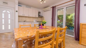 Een eetruimte met een ronde tafel en vier stoelen, een keuken op de achtergrond en een glazen schuifdeur naar een buitenruimte.