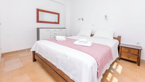 Een slaapkamer met een bed, nachtkastje, dressoir, spiegel en een wandlamp.
