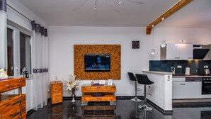 A modern kitchen with a built-in oven, a dining area with a bar stool, and a TV mounted on a textured wall. - Apartment Cicko (Trogir)