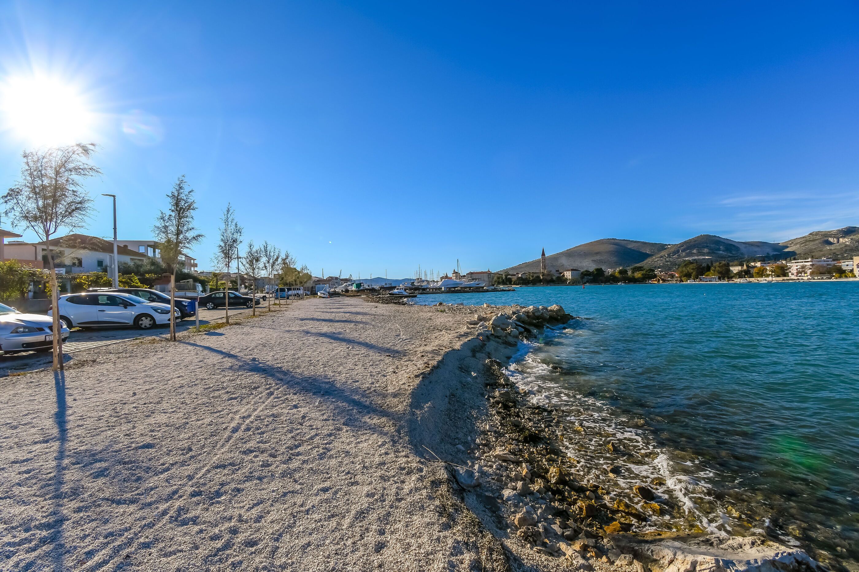 En strand med klart vatten, en stenig kustlinje och parkerade bilar.