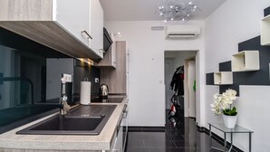 A modern kitchen with a built-in oven, a sink, and a stainless steel faucet. There is a small table with a potted plant beside the sink. - Apartment Cicko (Trogir)