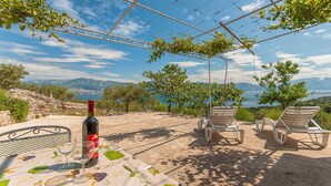 A table with a wine bottle and glass, two lounge chairs, and a view of the sea and mountains. - House Vela Lozna (Postira)