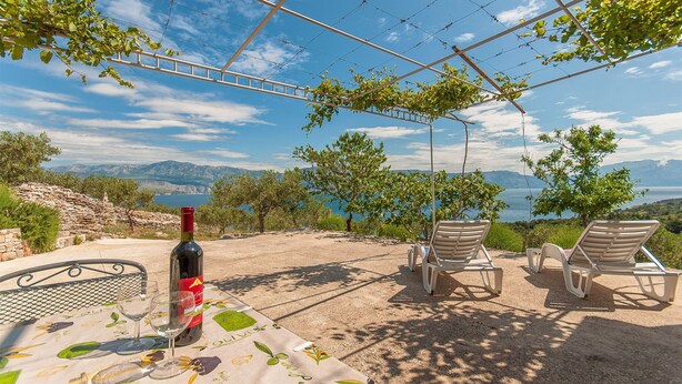 Ein Tisch mit Weinflasche und Glas, zwei Lounge-Stühle und Blick auf Meer und Berge.