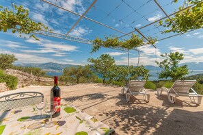 A table with a wine bottle and glass, two lounge chairs, and a view of the sea and mountains. - House Vela Lozna (Postira)