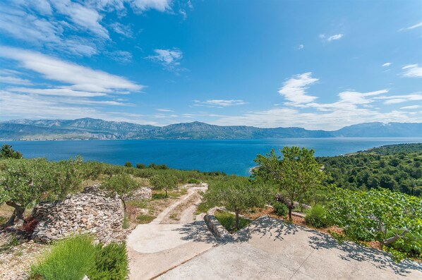 A coastal landscape with a clear sky, a stone pathway, and a view of the sea and mountains. - House Vela Lozna (Postira)