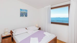 Een slaapkamer met een bed, een nachtkastje, een raam met uitzicht op zee en een schilderij aan de muur.