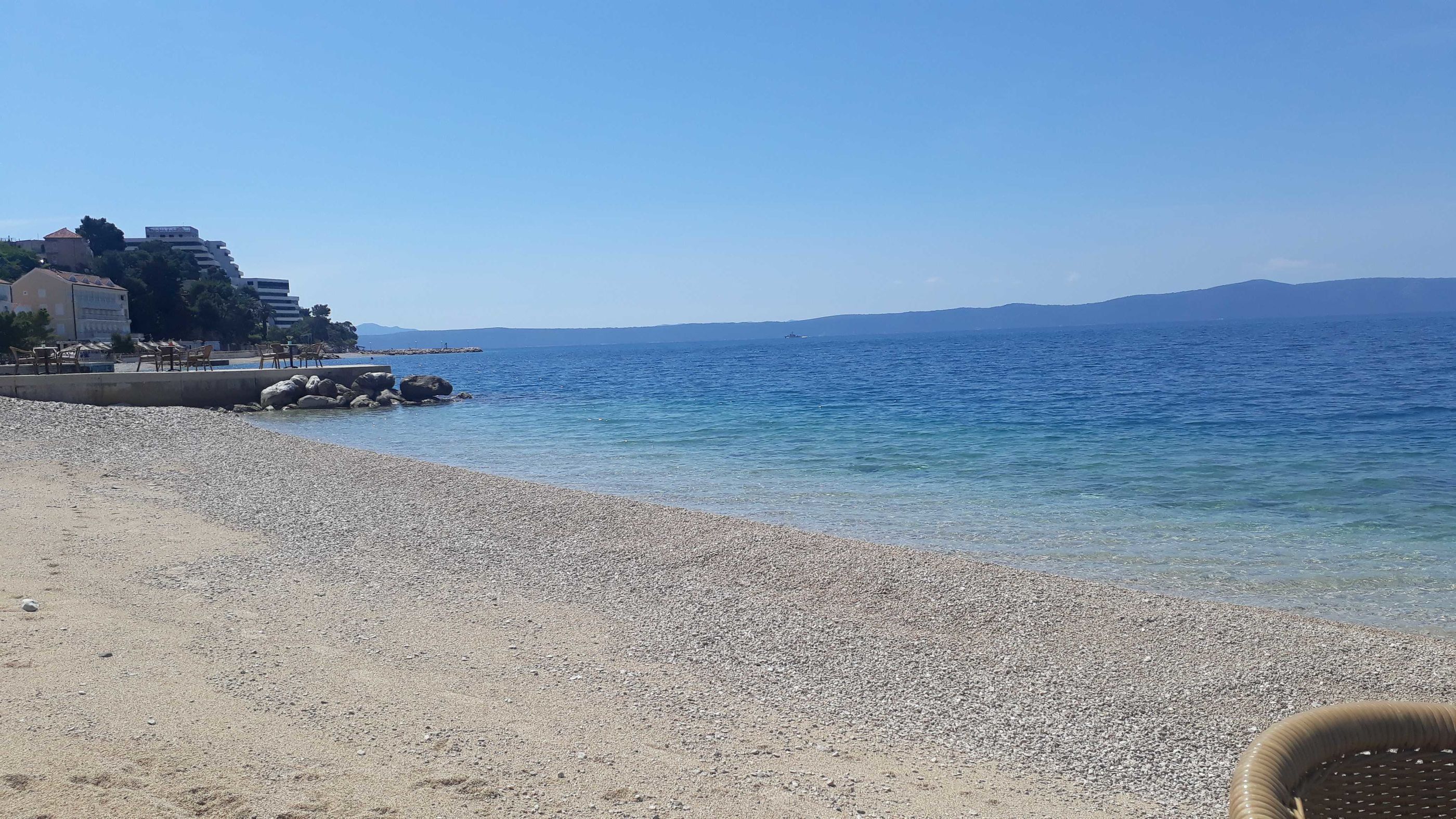Una playa de guijarros con una vista despejada del mar y montañas lejanas.