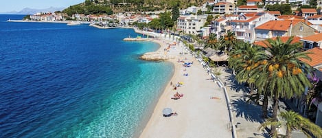 A coastal town with a beach, clear blue waters, and buildings with red-tiled roofs.