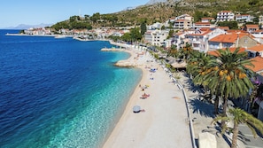 A coastal town with a beach, clear blue waters, and buildings with red-tiled roofs. - Apartments Branka (Podgora)