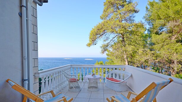 Ein Balkon mit Korbstühlen und einem kleinen Tisch, mit Blick aufs Meer.