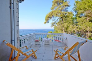 Ein Balkon mit Korbstühlen und einem kleinen Tisch, mit Blick aufs Meer.