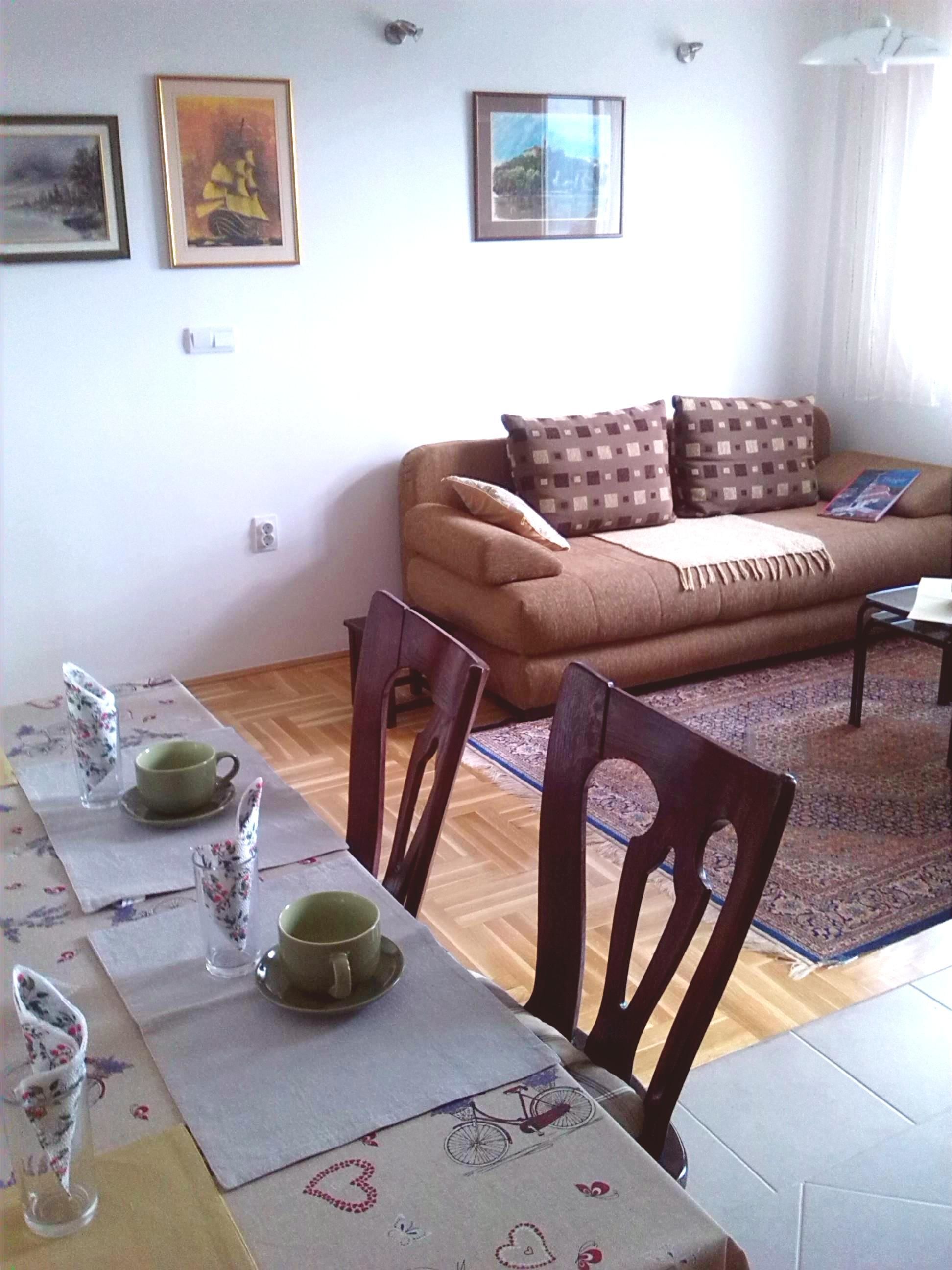 A living room with a sofa, a dining table set with cups and saucers, and two framed pictures on the wall.