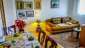 Ein Wohnzimmer mit einer Couch, einem Esstisch gedeckt mit grünen Tassen und Untertassen sowie einer Vase mit roten Blumen.