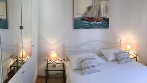 Ein Schlafzimmer mit einem Bett, zwei Nachttischen mit Lampen, einem Spiegel und einem Gemälde eines Segelbootes an der Wand.