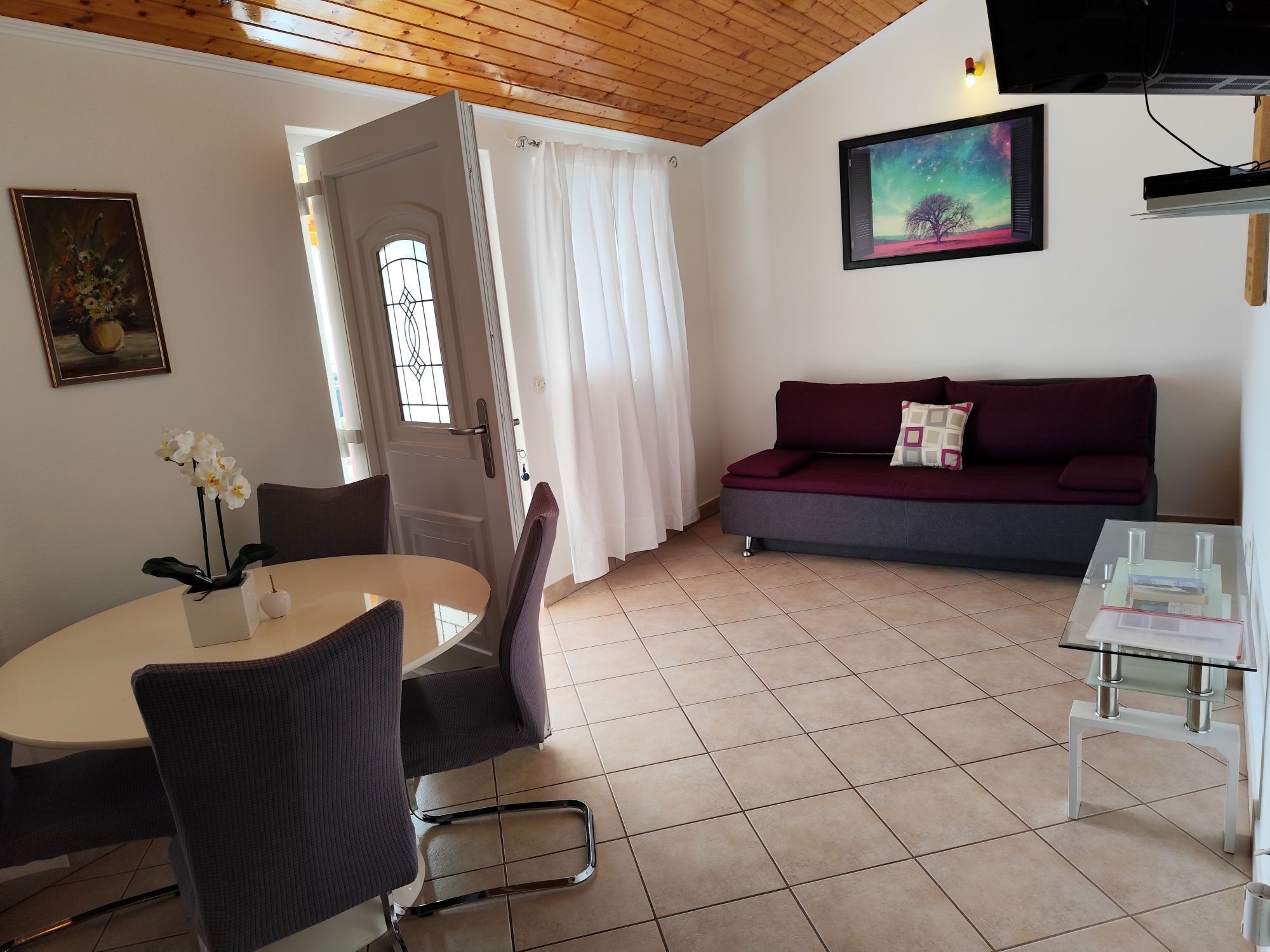 A living room with a sofa, a dining table with chairs, a TV, and a painting on the wall.