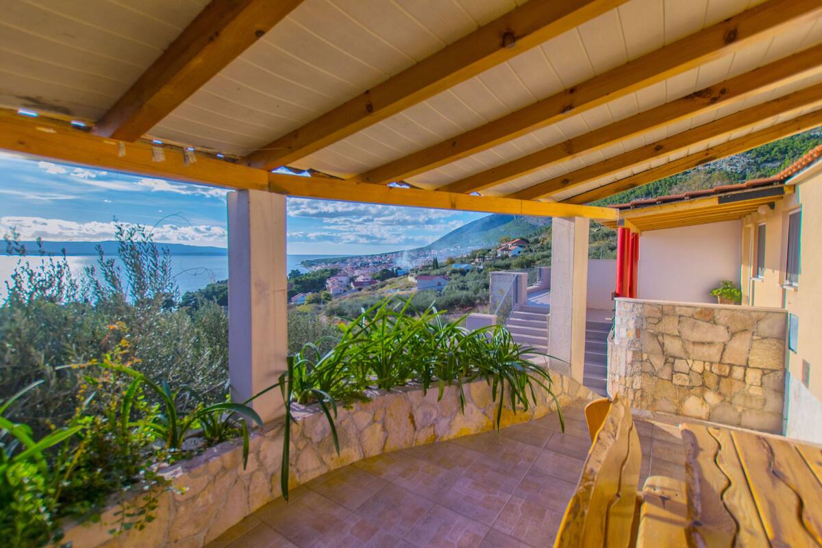 Un espacio al aire libre cubierto con pared de piedra, banco de madera y vistas a un pueblo costero y montañas.