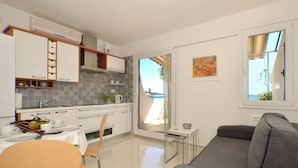 A modern kitchen with white cabinets, a dining table set for two, and a grey sofa in the living area. - Apartments Inge (Seget)