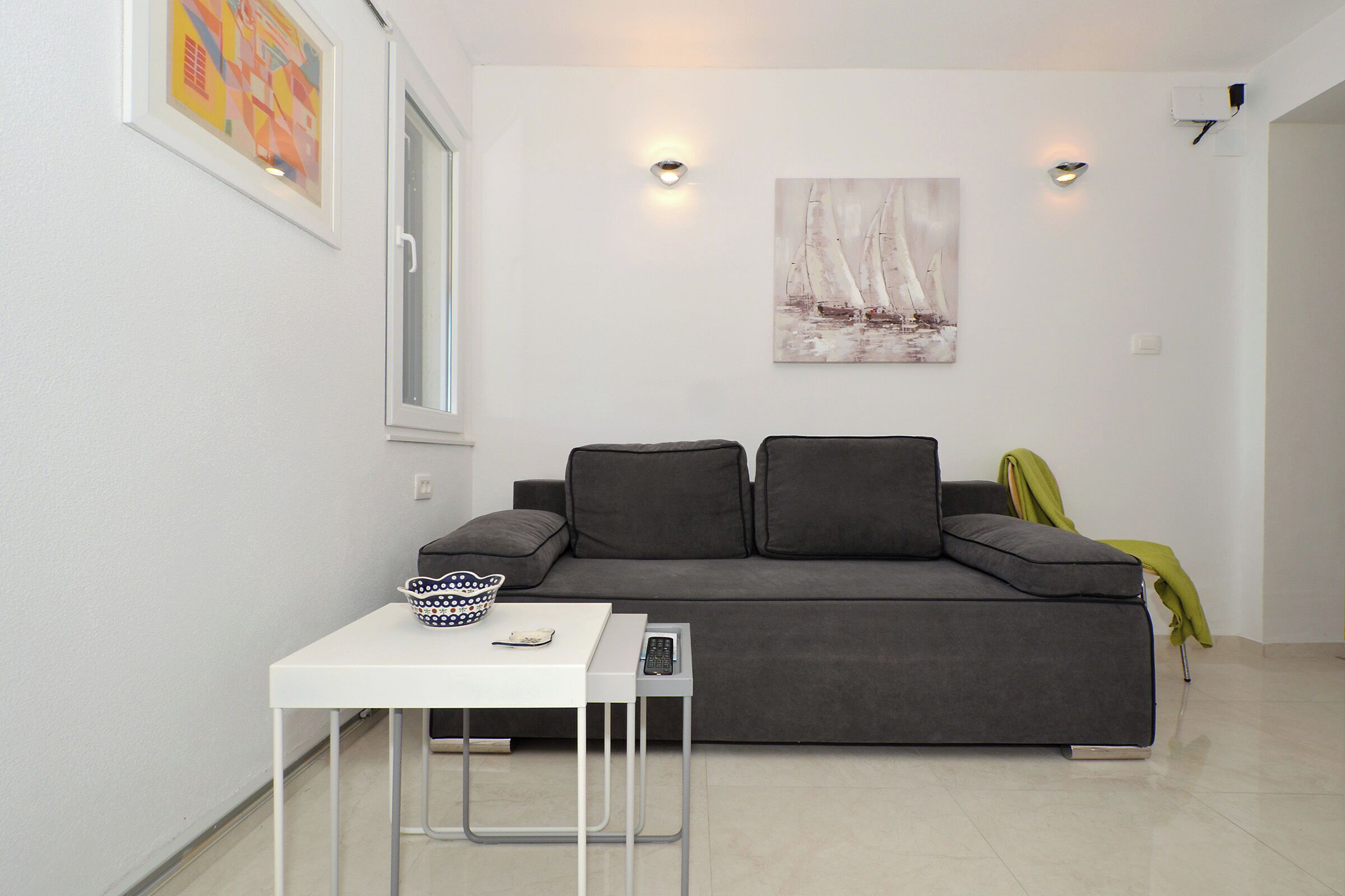 A modern living room with a grey sofa, a white coffee table, and a painting of sailboats on the wall.