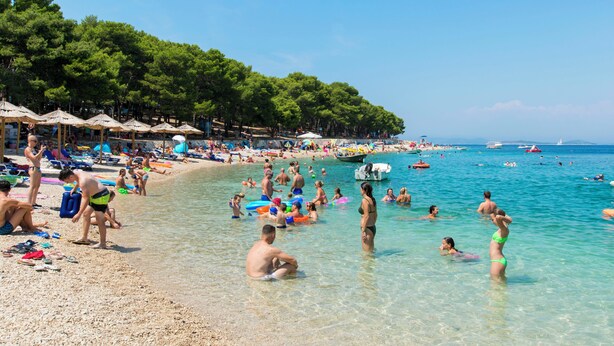 Una spiaggia affollata con acque poco profonde e cristalline, ombrelloni e persone che si godono il sole.