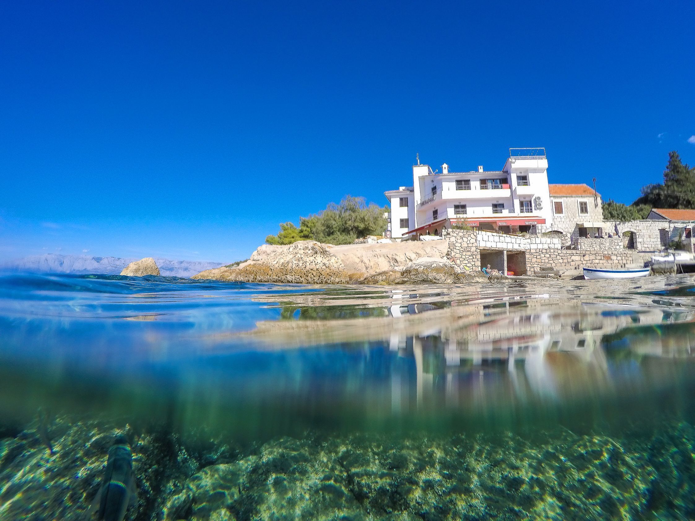 A coastal building with a stone facade, a red roof, and a clear view of the sea.