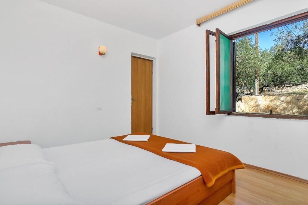 Een slaapkamer met een bed, een raam met uitzicht op bomen en een houten deur.