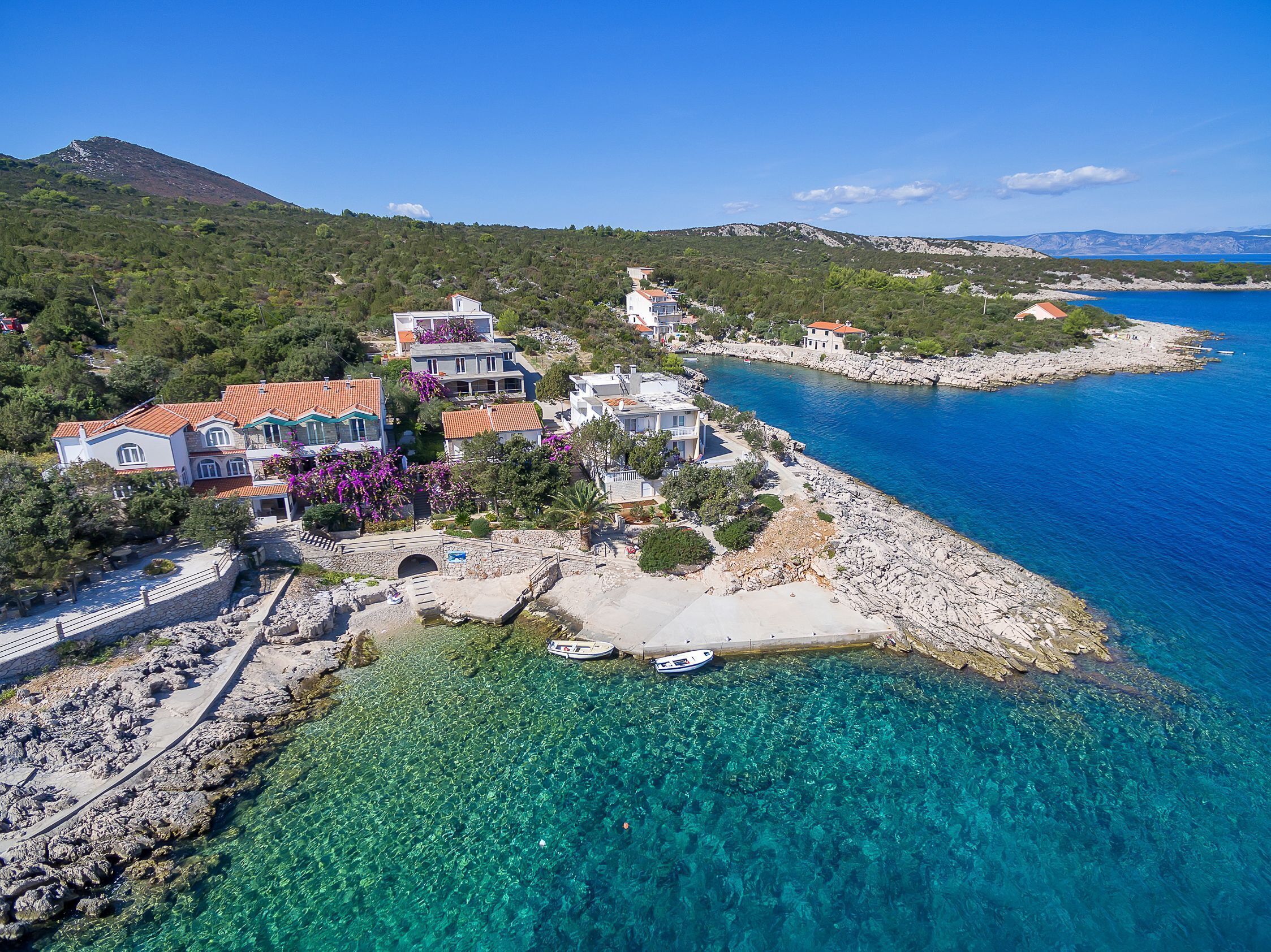 A coastal village with houses along the shoreline, clear blue waters, and a mountain in the background.