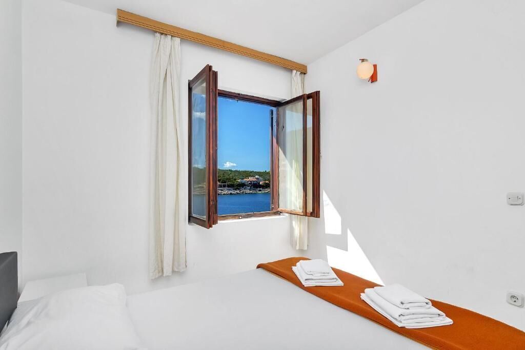 A hotel room with a bed, a window with curtains, a view of the sea, and a small table with towels.
