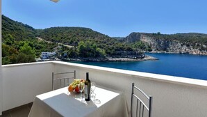 Un balcon avec une table dressée pour deux personnes, offrant une vue sur un paysage côtier avec des falaises et une étendue d’eau.