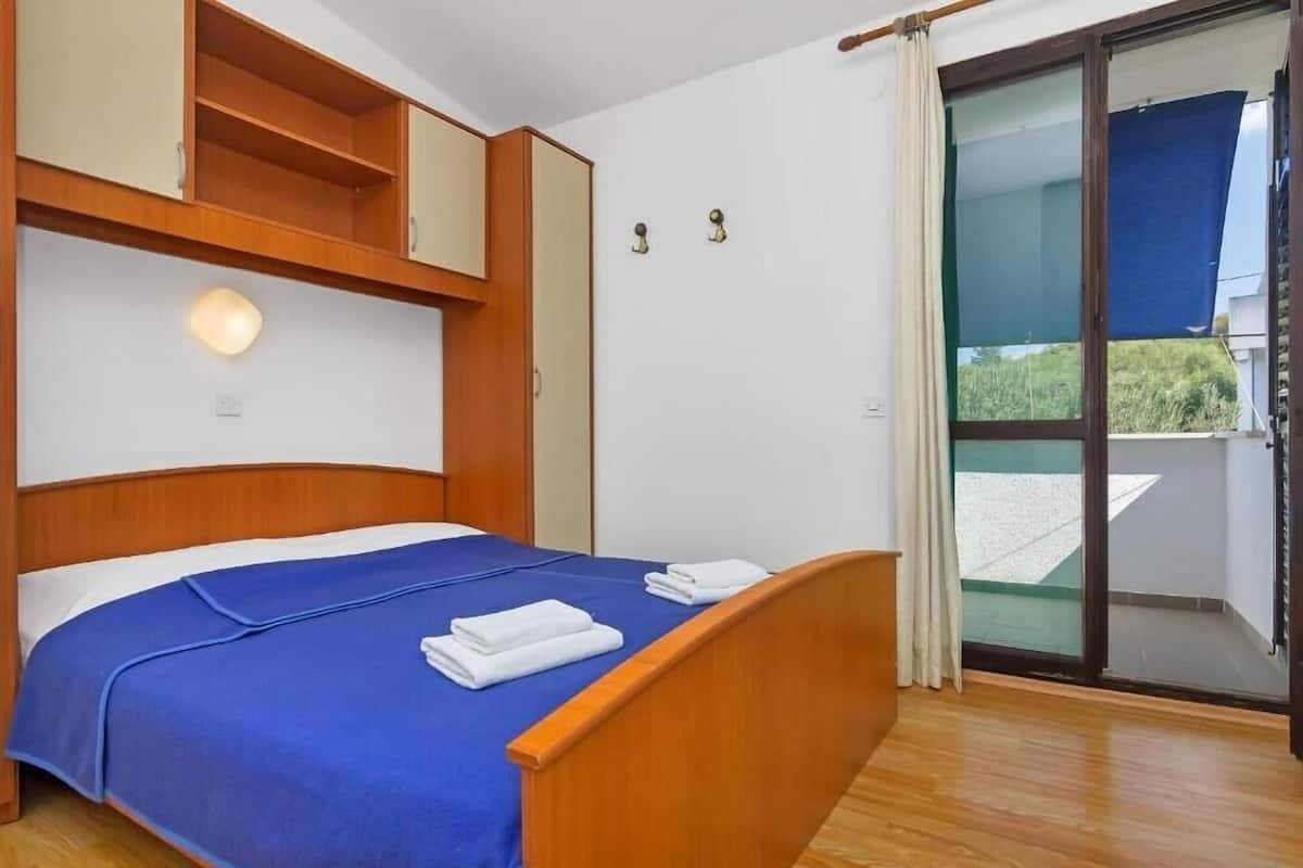 Ett hotellrum med en säng, en sänggavel i trä, inbyggda hyllor, en skjutdörr i glas som leder ut till balkongen och en väggmonterad lampa.
